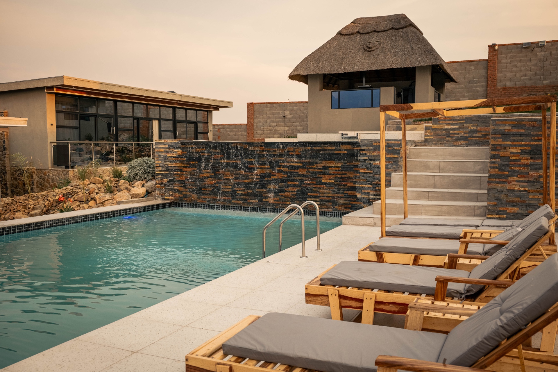 Lions Gate Villas pool at dusk with sun loungers and a stone water feature